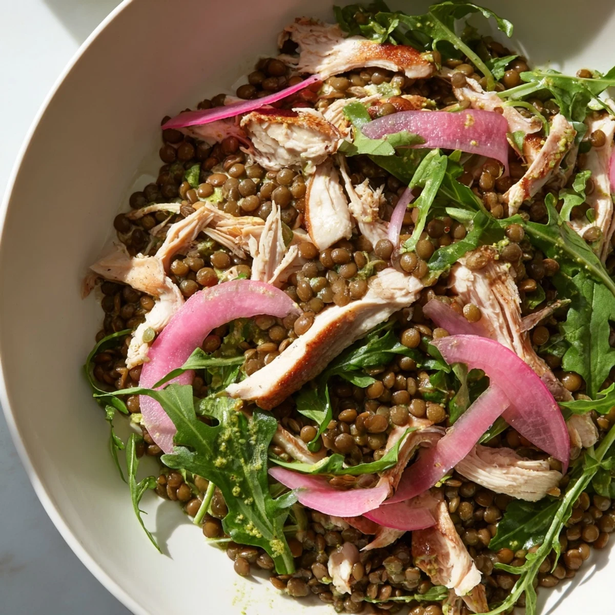 A close-up of the Lentil & Chicken Spring Salad with tender lentils, juicy shredded chicken, peppery arugula, and bright pickled onions in a mustard dressing.