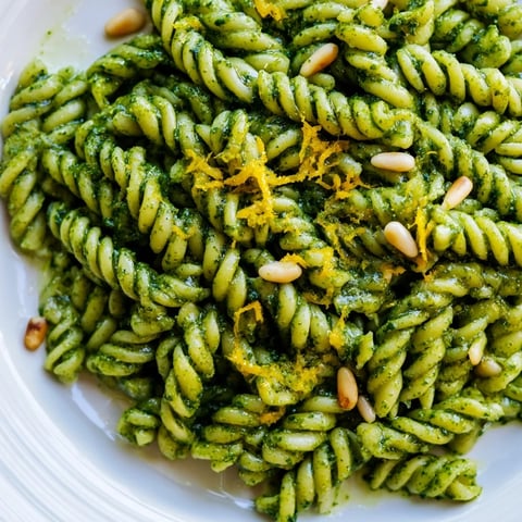 Vibrant Spring Green Pesto Pasta Salad in a white bowl, showcasing glossy fusilli coated in basil pesto and topped with peas, arugula, and toasted pine nuts.