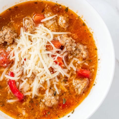 Hearty Pizza Soup in a white bowl with red bell peppers, onions, and gooey mozzarella, ready to be served with crusty bread.  