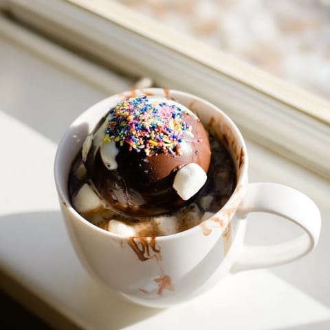 In a cozy mug, a hot chocolate bomb melts into creamy cocoa with mini marshmallows floating in rich, steaming milk.