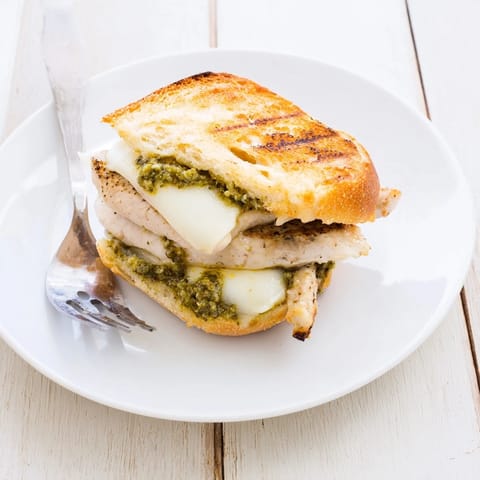 A toasted ciabatta roll holds juicy chicken with creamy pesto and gooey mozzarella, served with sliced tomatoes for the Pesto Chicken Melt.