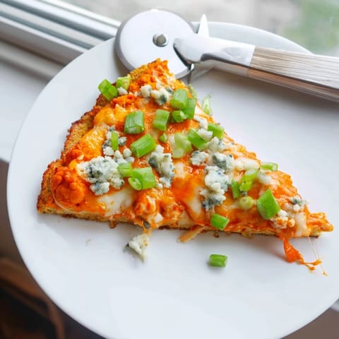 Close-up of a slice of Buffalo Cauliflower Pizza, showcasing crispy edges and tangy buffalo sauce drizzle.  