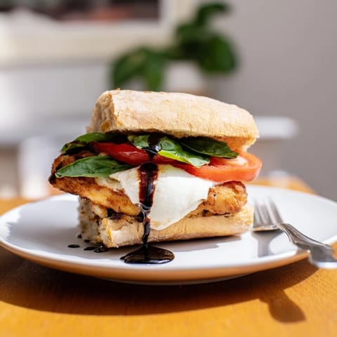 Crispy golden chicken cutlets layered with creamy mozzarella, fresh basil, and juicy tomato on a toasted ciabatta roll, served warm for a satisfying Italian-American meal.