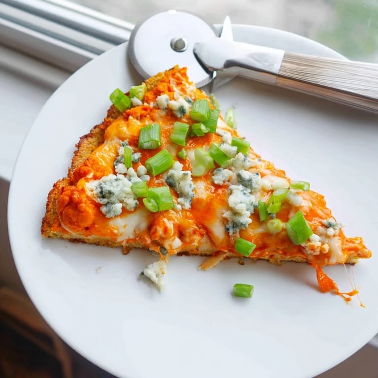 Close-up of a slice of Buffalo Cauliflower Pizza, showcasing crispy edges and tangy buffalo sauce drizzle.  